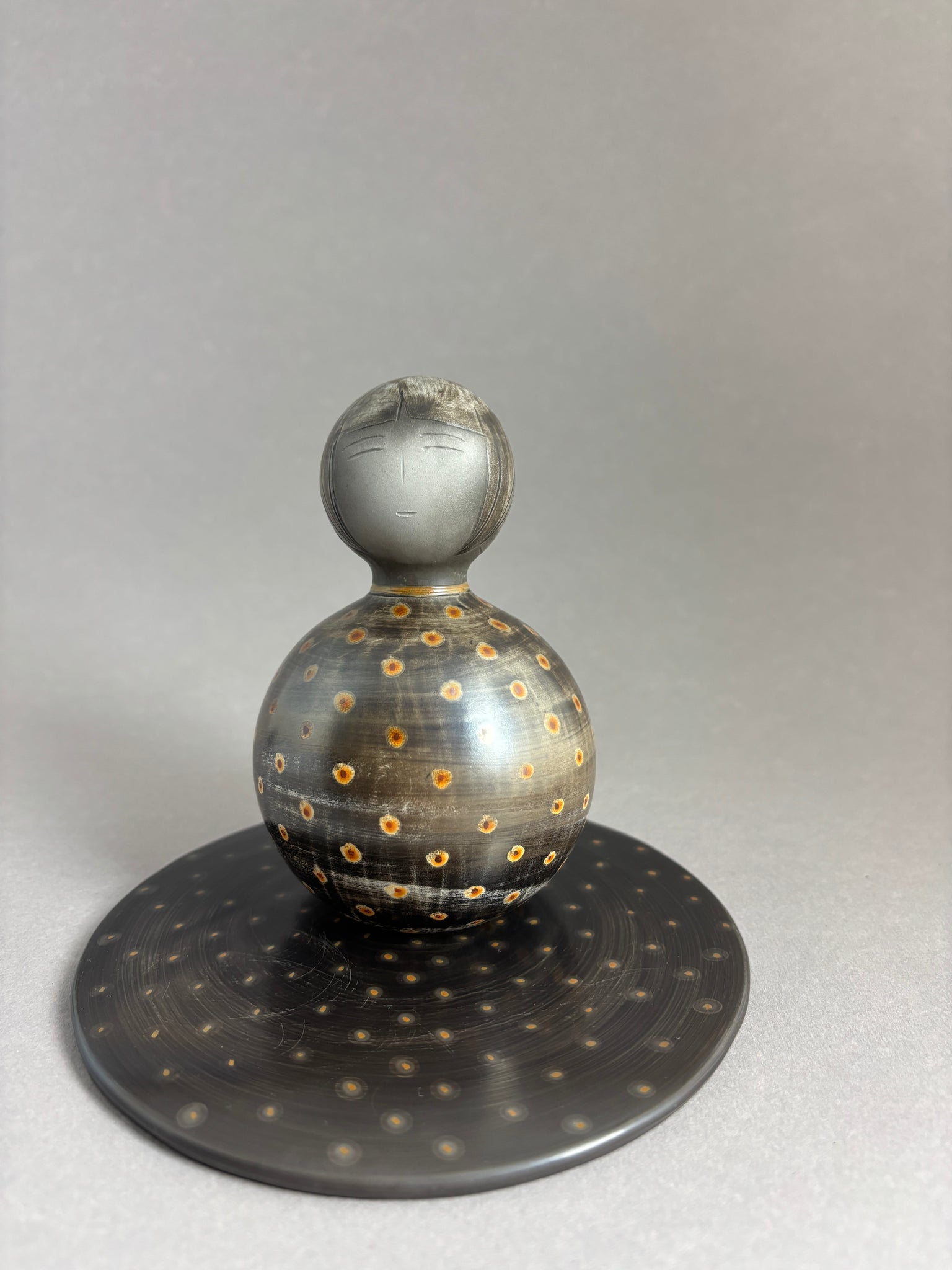 Kokeshi boule gris foncé aux pois colorés sur socle plat